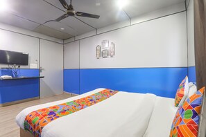 Quarto de hotel com cama, escrivaninha, televisão e ventoinha no teto.