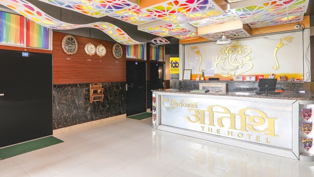 A hotel reception area with a modern design, including a reception desk, a clock, and a decorative ceiling. - Fabexpress Atithi (Nagri)