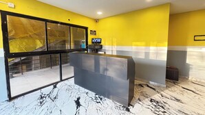 Ein Empfangsbereich mit Marmorboden, einer Rezeption, einem Fernseher und einer sichtbaren Treppe durch eine Glastür.