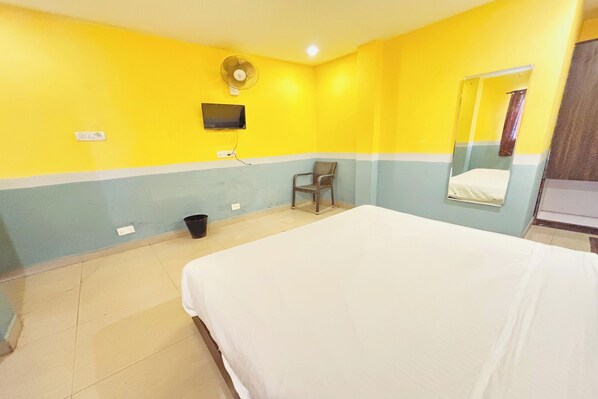 A hotel room with a bed, a chair, a fan, a TV, and a mirror. - 29 Beach House Goa (Morjim)