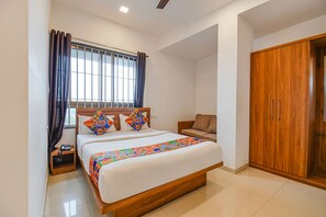 A bedroom with a wooden bed, a nightstand, a wardrobe, and a window with curtains. - Fabhotel The Address (Nashik)