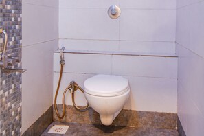 A bathroom with a toilet, a shower, and a tiled wall. - Fabhotel The Address (Nashik)