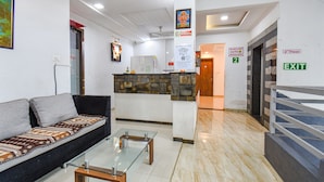 Un hall de hotel con un sofá, una mesa de vidrio, una recepción y un letrero de salida.