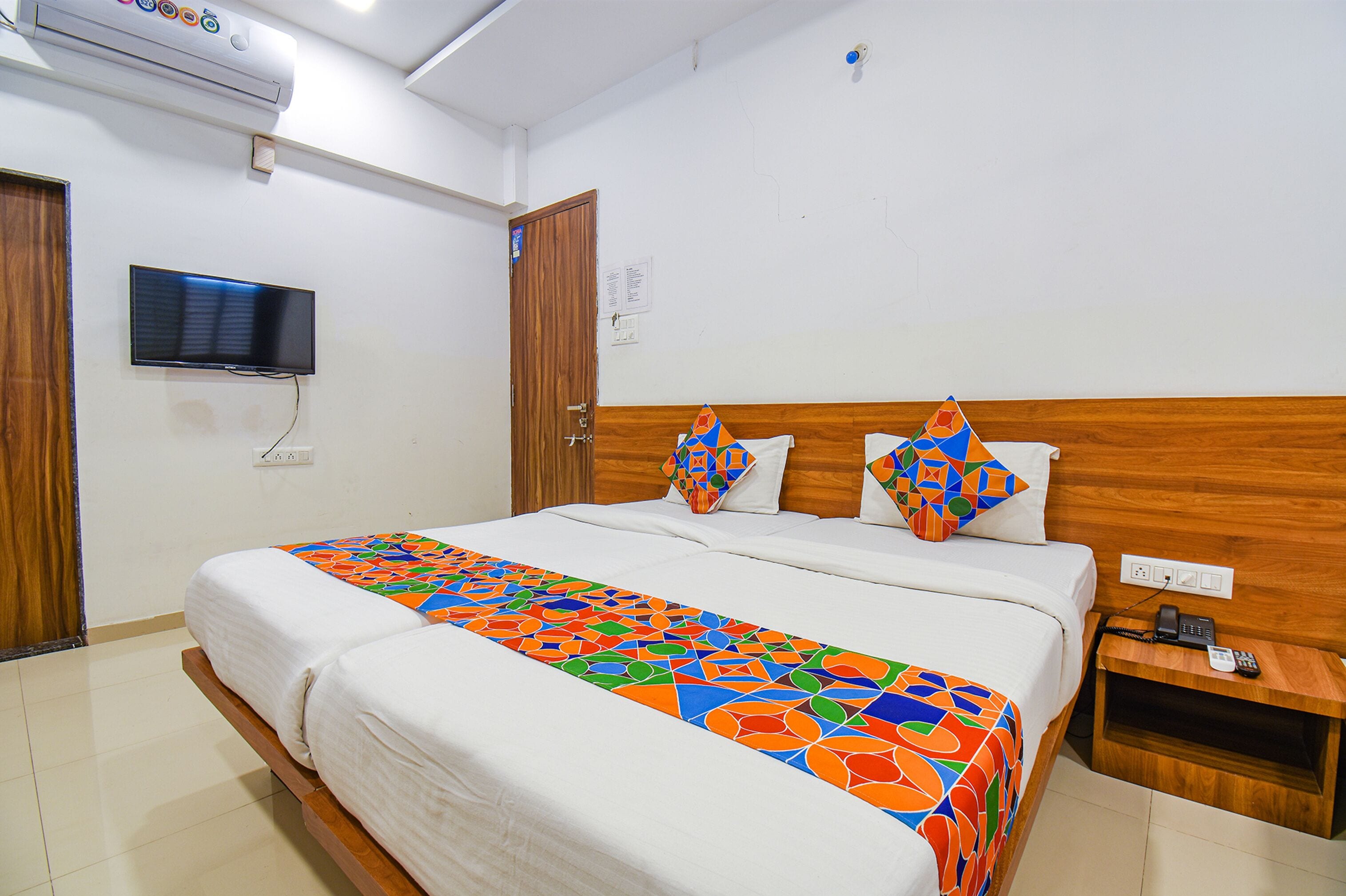 A hotel room with a large bed, a television mounted on the wall, and a wooden headboard.