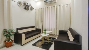 A living room with a sofa, a small round table, a potted plant, and a decorative wall piece. - Fabhotel Paradise Stay Inn (Nagpur)