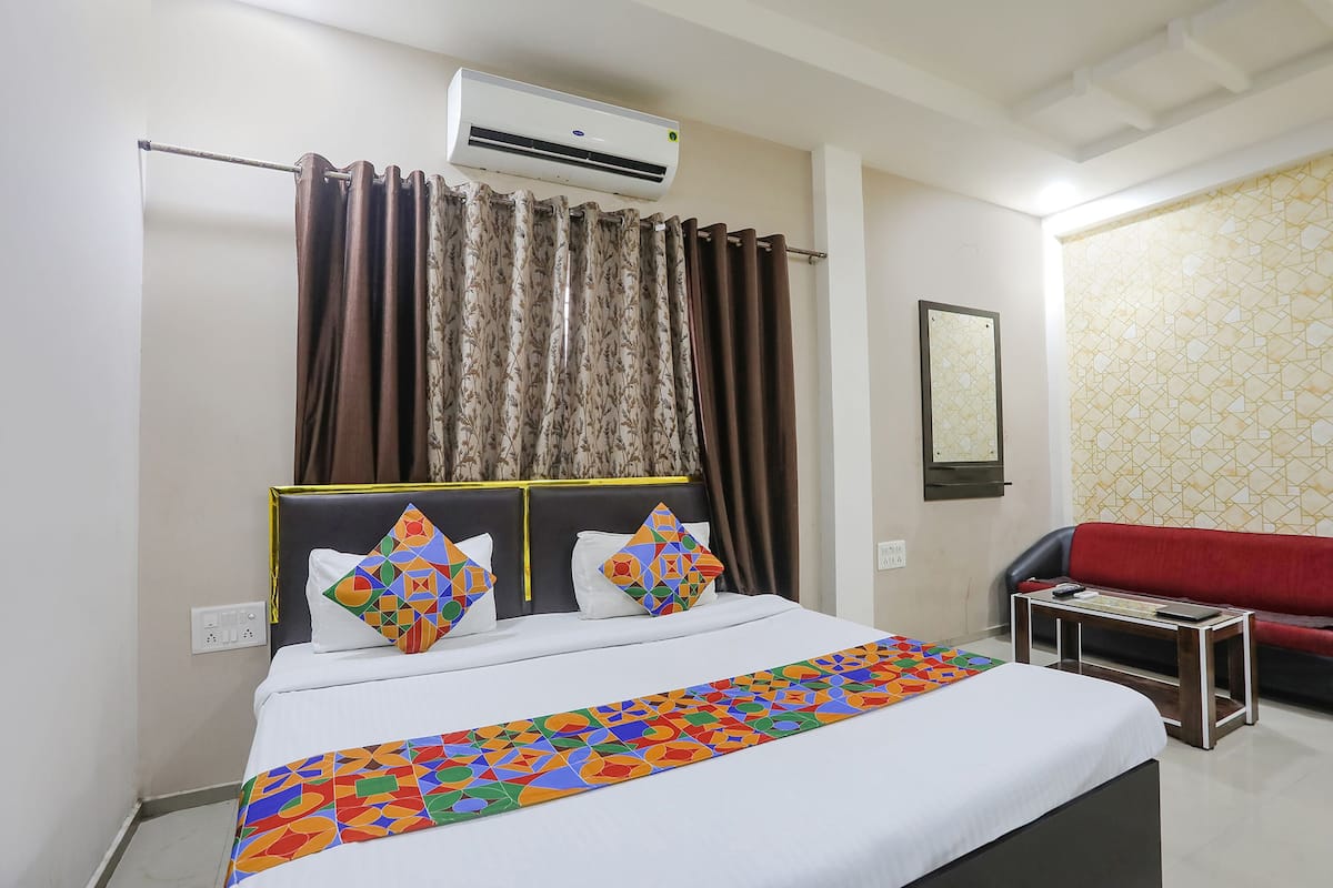 A hotel room with a bed, an air conditioner, a red sofa, and a patterned wall.