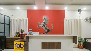 A hotel reception desk with a red wall, a mounted horse sculpture, a reception counter, a potted plant, and a sign reading "fab hotels". - Fabhotel Paradise Stay Inn (Nagpur)