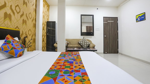 A hotel room with a neatly made bed, a sofa, a small table, and a door. - Fabhotel Paradise Stay Inn (Nagpur)