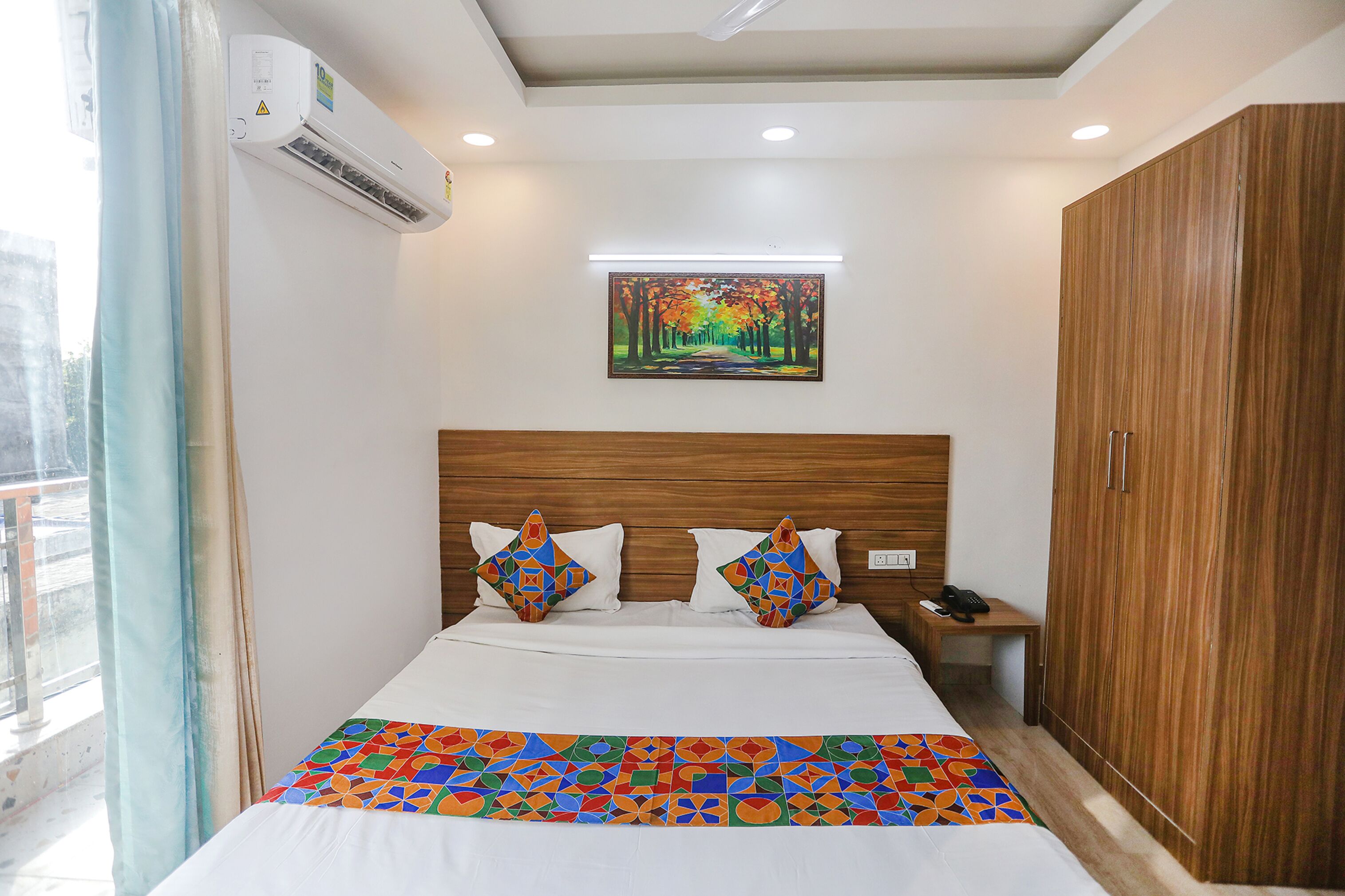 Una habitación de hotel con cama, mesita de noche, armario y un cuadro en la pared.