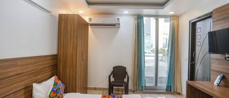 Een hotelkamer met een bed, een stoel, een televisie en een airconditioning.