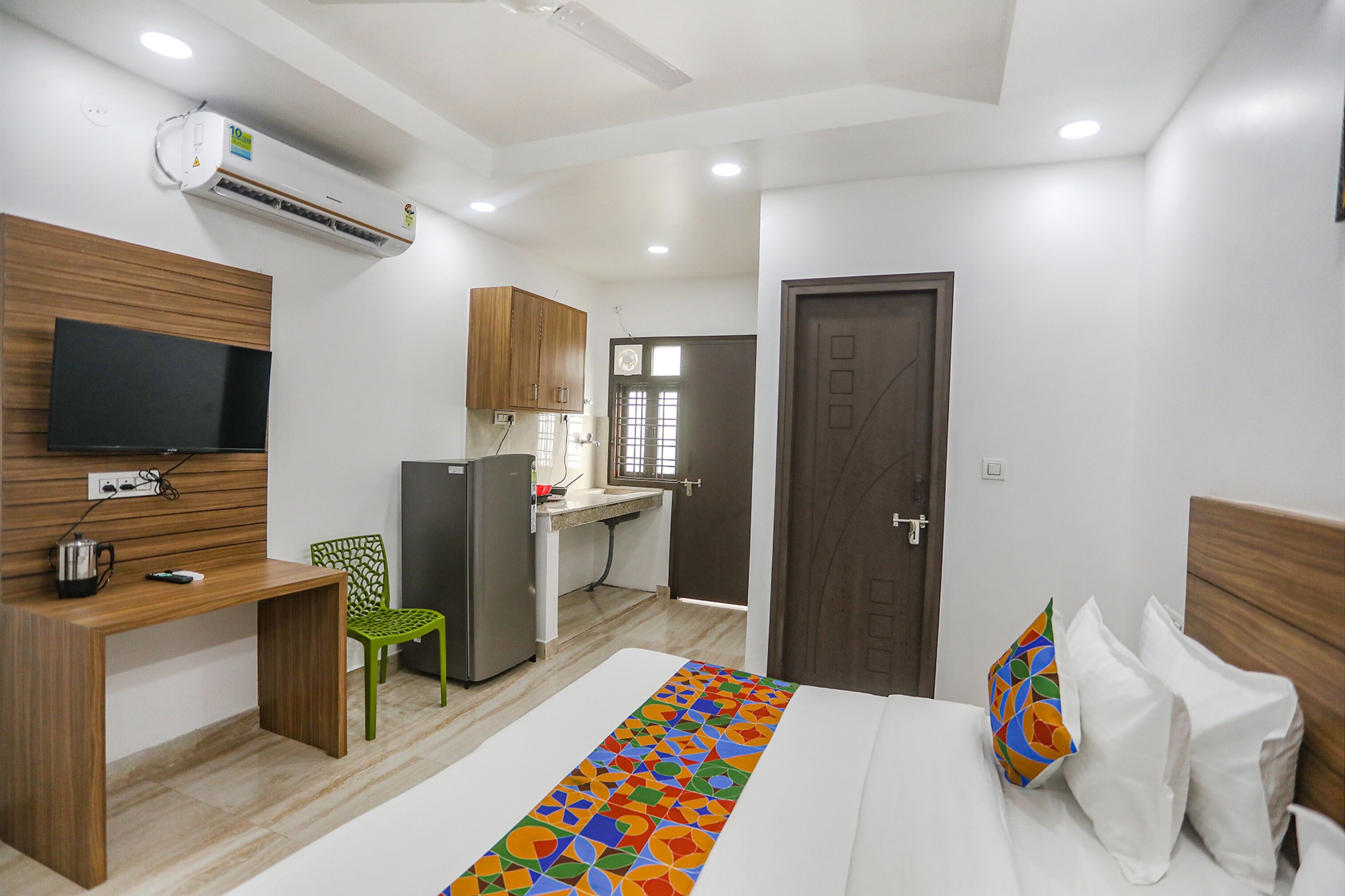 A hotel room with a bed, a desk, a chair, a television, a refrigerator, and a small kitchenette.