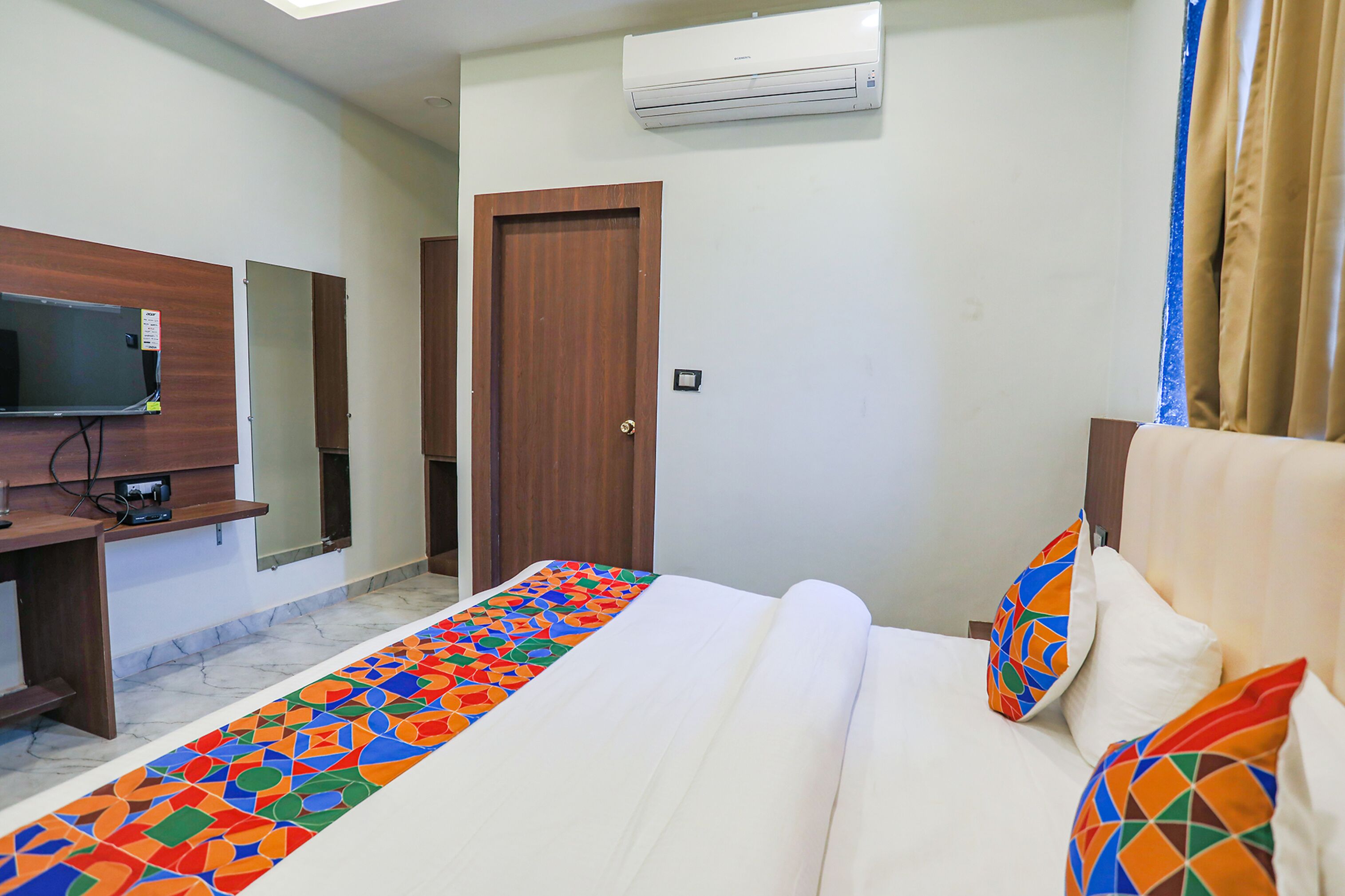A hotel room with a bed, a TV, a wooden door, and an air conditioning unit.