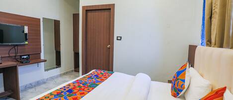 A hotel room with a bed, a TV, a wooden door, and an air conditioning unit.