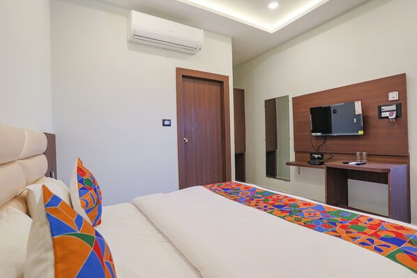 A hotel room with a bed, a TV on a wooden stand, and an air conditioner on the wall. - Fabhotel Dds (Lucknow)