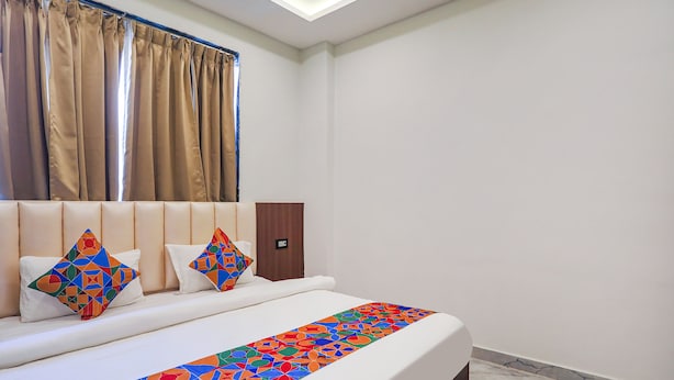 A hotel room with a bed, a headboard, a nightstand, and a window with curtains. - Fabhotel Dds (Lucknow)