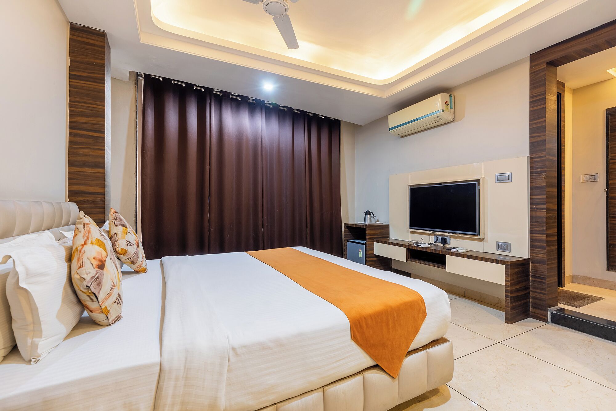 A modern hotel room with a large bed, a flat-screen TV, an air conditioning unit, and a ceiling fan.