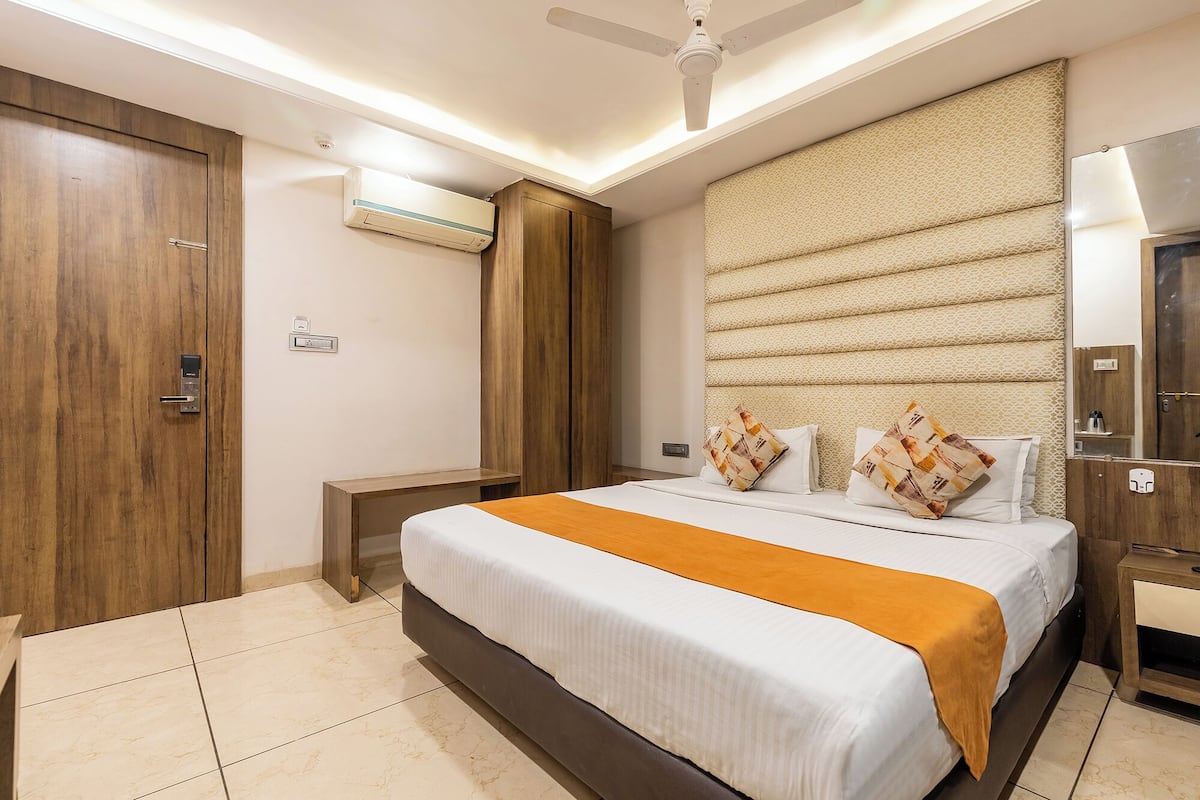 Quarto de hotel com cama, mesa de cabeceira, guarda-roupa, ventoinha no teto e ar condicionado.