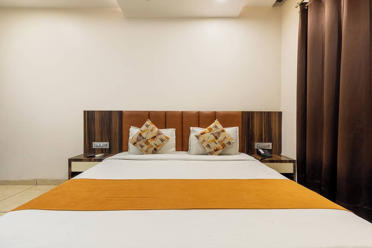 Quarto de hotel com uma cama grande, duas mesas de cabeceira, um telefone e uma cortina marrom.