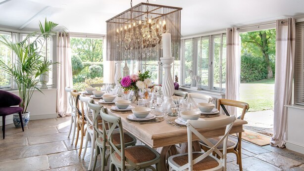 Comedor con una mesa de madera dispuesta para seis personas, rodeada de sillas blancas con asientos de mimbre.
