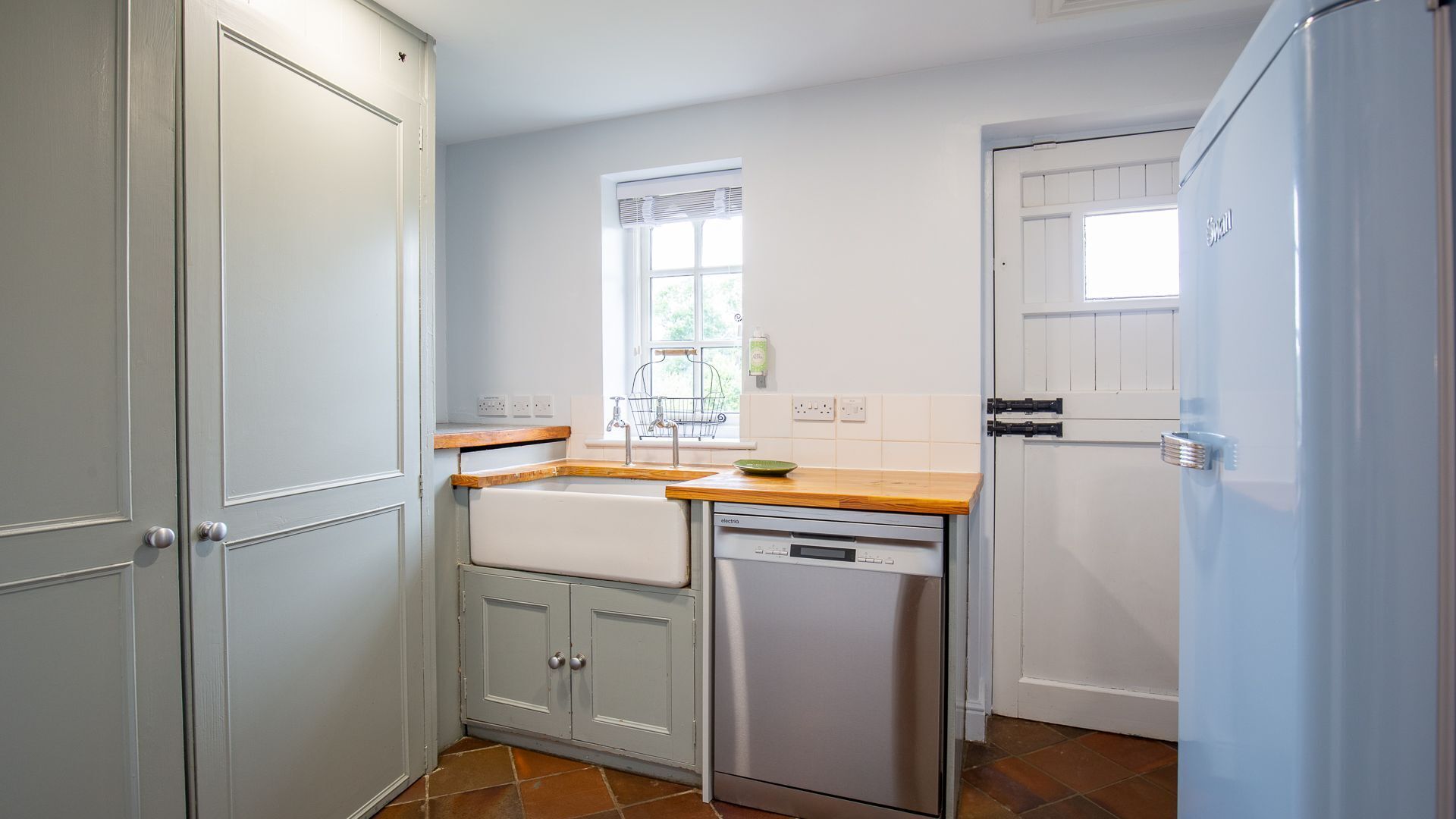A compact kitchen with a dishwasher, a window with blinds, and a door with a handle.