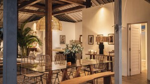 Un comedor con una mesa de vidrio, sillas de mimbre y un banco de madera.