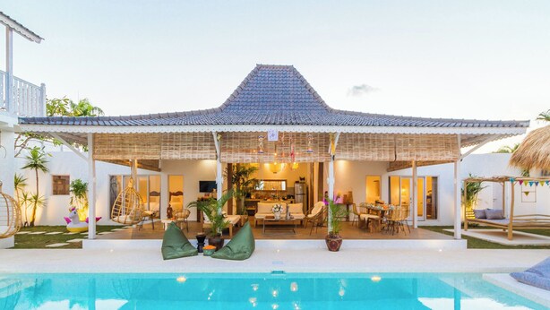 Una casa con piscina, un área de estar techada al aire libre y una cocina visible a través de la puerta abierta.
