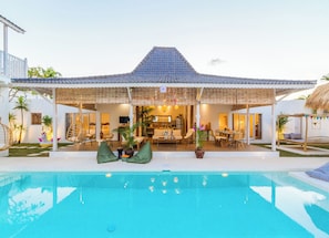 Uma casa com piscina, área de estar coberta ao ar livre e cozinha visível pela porta aberta.