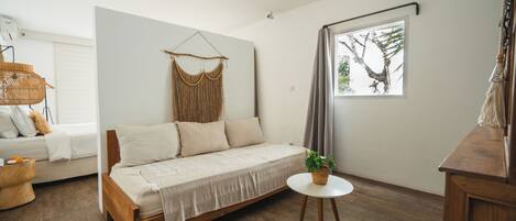 A modern living room with a wooden sofa, a small round table with a plant, and a large window with a tree view.