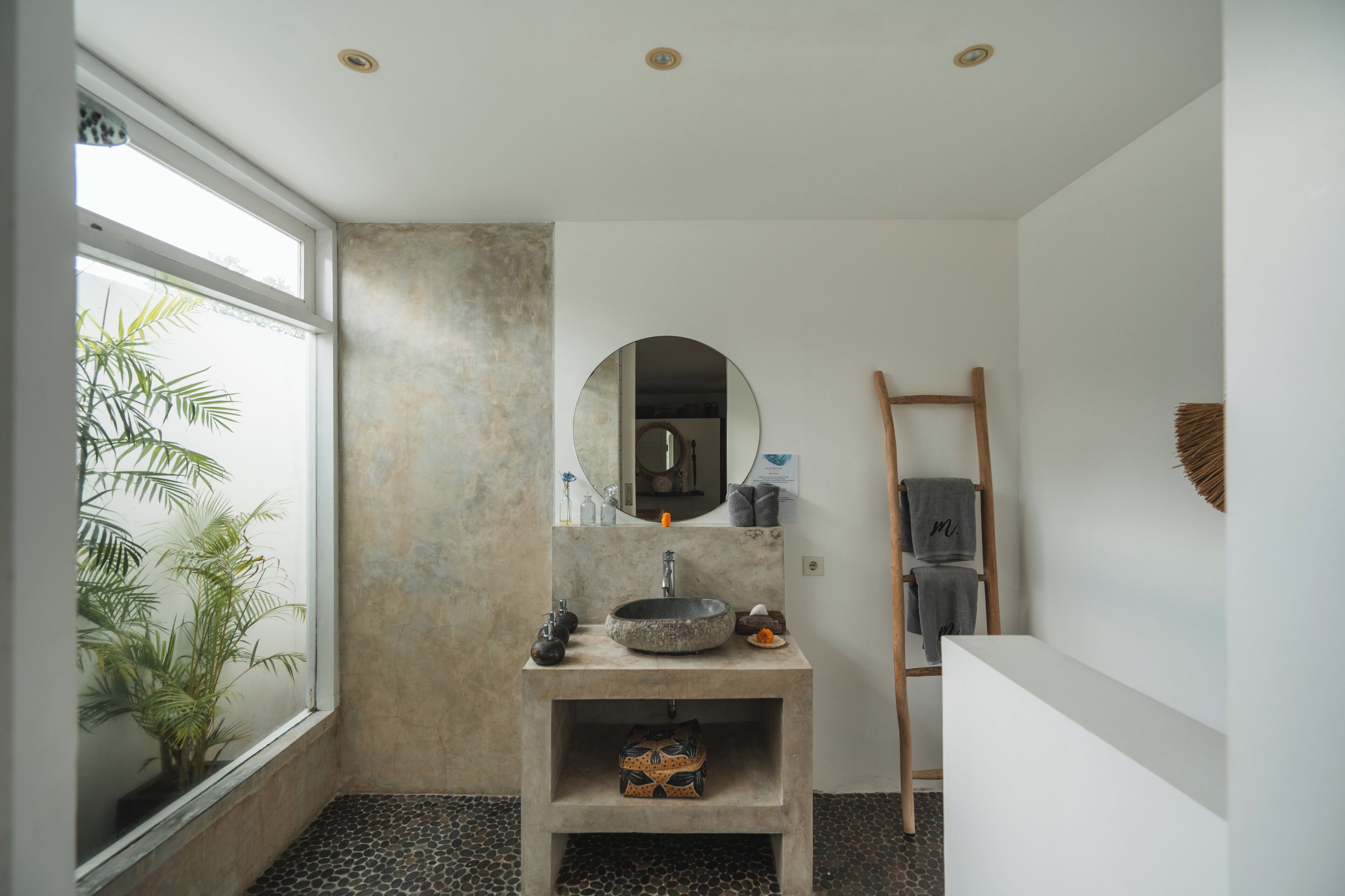 A bathroom with a round mirror, a sink, a towel rack, and a plant.