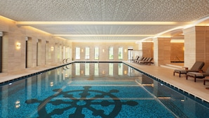 A large indoor swimming pool with a decorative pattern on the floor, surrounded by lounge chairs and a sunbed. - Ayan Zalaat (Ulaanbaatar)