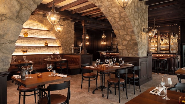 A restaurant with stone walls, wooden beams, and hanging light fixtures. Tables are set with wine glasses and cutlery. - Ayan Zalaat (Ulaanbaatar)