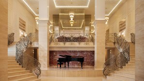 A grand lobby with a piano, ornate staircases, and a chandelier. - Ayan Zalaat (Ulaanbaatar)