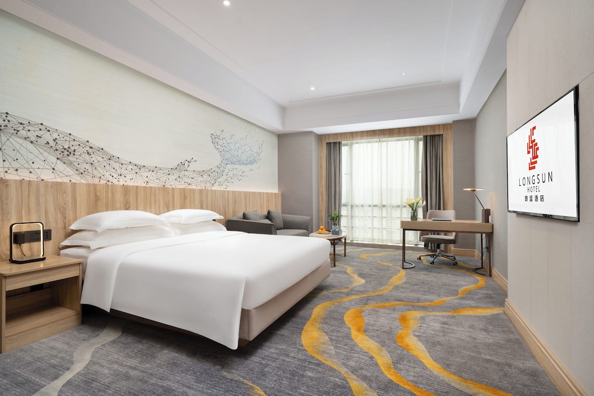A hotel room with a large bed, a desk, a chair, a nightstand, a wall art piece, and a framed sign on the wall.
