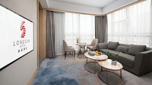 A modern hotel room with a grey sofa, two armchairs, a small round table, and a TV displaying the hotel's name. - Langson Dongguan - Dalang Songshan Lake (Dongguan)