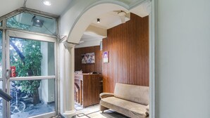 Zona de recepción con un revestimiento de madera, un sofá color beige y una puerta de vidrio que da al exterior.