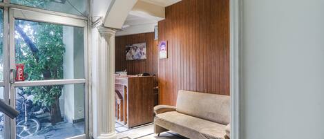 A reception area with a wooden panel wall, a beige sofa, and a glass door leading outside.
