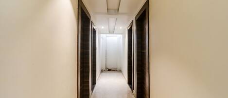A narrow, well-lit hallway with dark wooden doors on either side and a plain white wall.
