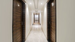 A hallway with wooden doors and a tiled floor, leading to a room with a white ceiling and recessed lighting. - Fabhotel Bless Inn (Prayagraj)