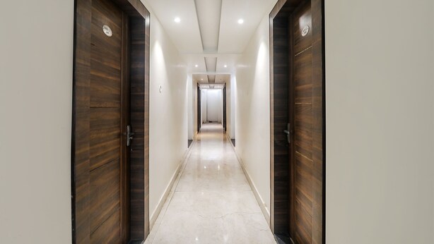 Un pasillo con puertas de madera y suelo de baldosas que conduce a una habitación con techo blanco e iluminación empotrada.