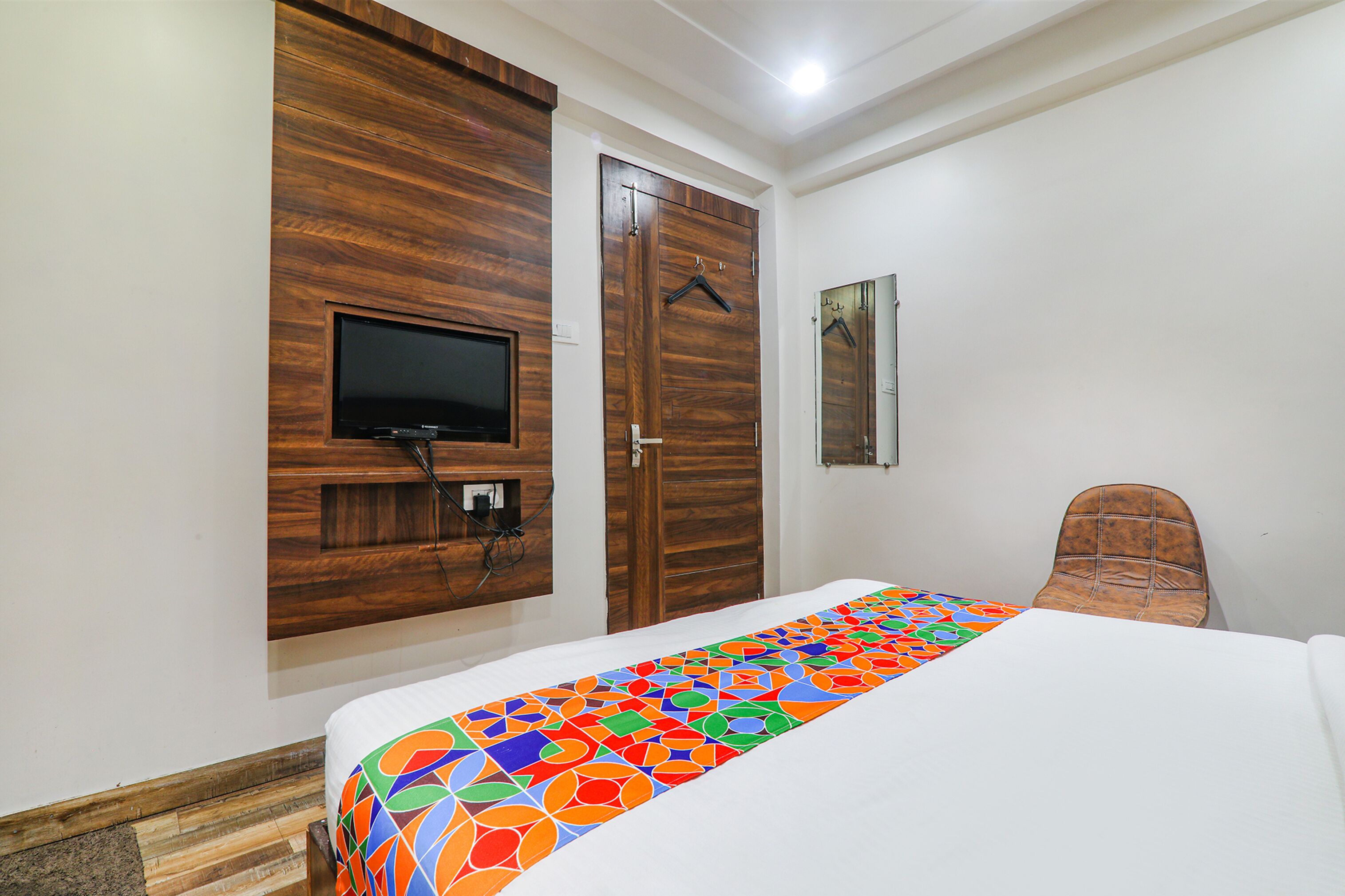 A bedroom with a bed, a TV mounted on the wall, a chair, and a wardrobe.