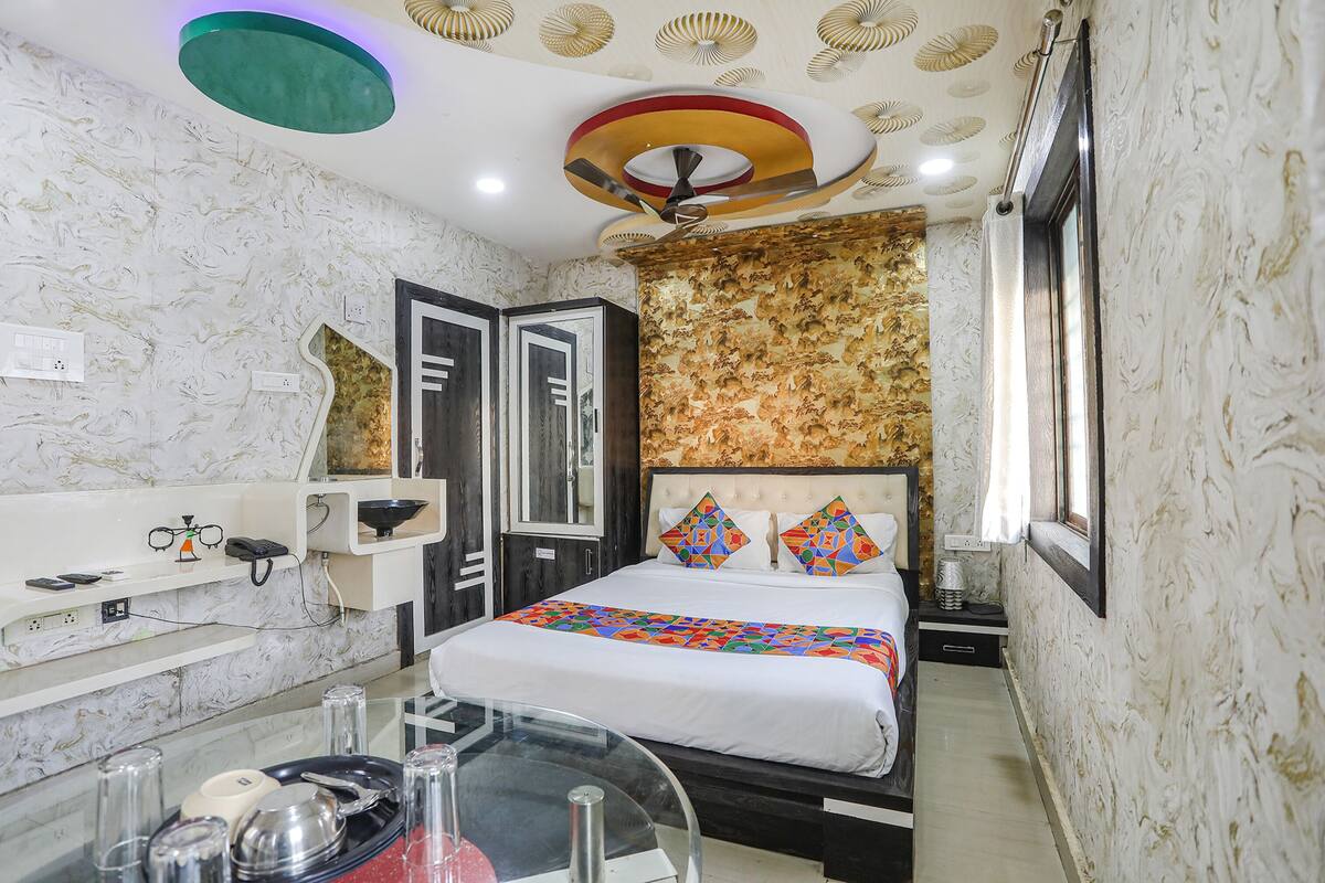 A hotel room with a bed, bedside table, and a mirror.