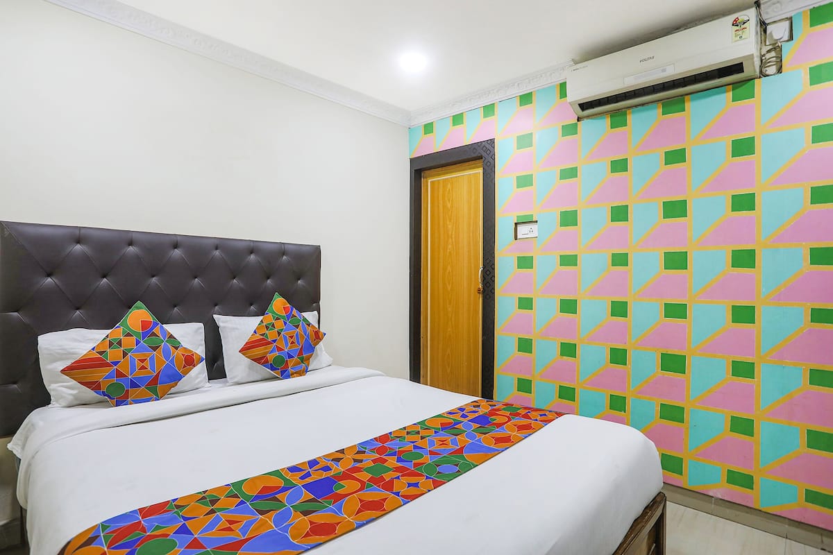 A hotel room with a bed, a decorative headboard, a colorful wall pattern, and an air conditioning unit.