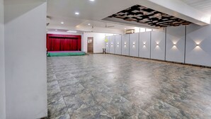 A spacious hall with a stage, seating, and a ceiling with exposed beams and recessed lighting. - Fabhotel Heritage Palace (Chhatrapati Sambhajinagar)