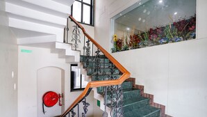 A staircase with ornate metal railings and a wooden handrail, leading to a reception area with a red fire hose mounted on the wall. - Fabhotel Heritage Palace (Chhatrapati Sambhajinagar)
