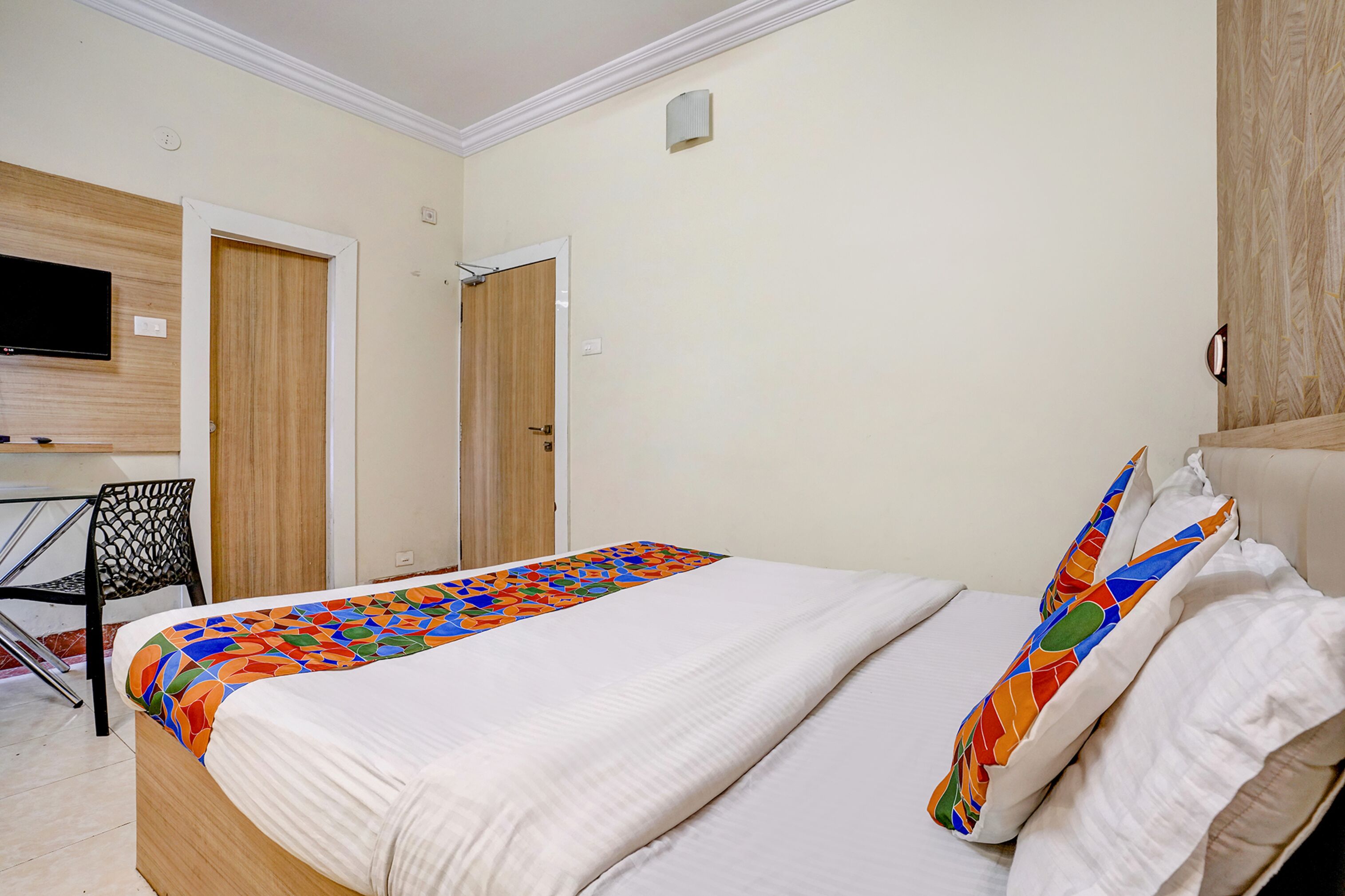 Quarto de hotel com cama, televisão na parede, escrivaninha e uma cadeira.