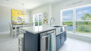 A modern kitchen with a large island, white cabinetry, and a view of greenery outside. - Sea La Vie- Dog Friendly Cottage in Orange Beach (Orange Beach)