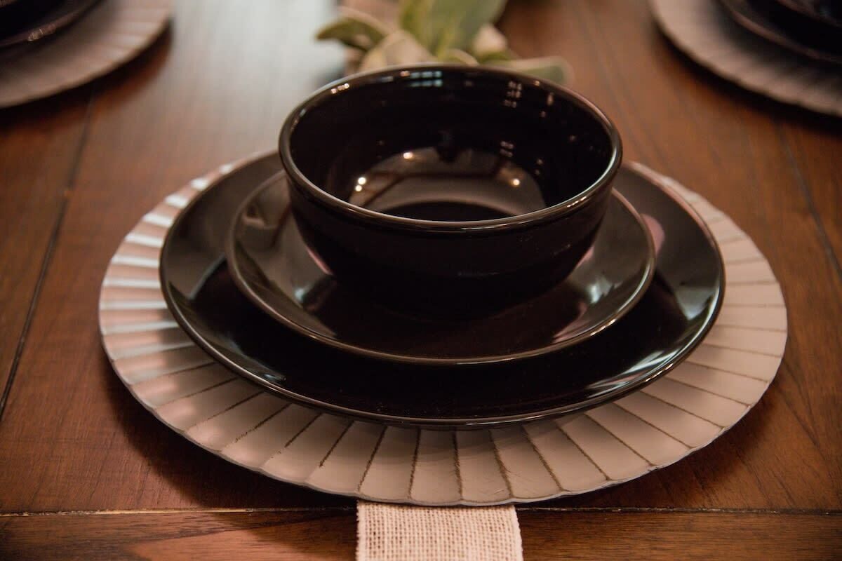 A dark-colored bowl on a matching plate, placed on a wooden table with a striped placemat.