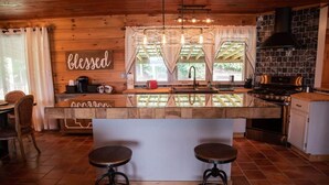 Een houten interieur met een keukeneiland, barstoelen en een bordje met de tekst 'gezegend'.