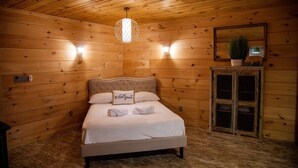 Een houten kamer met een bed, een nachtkastje, een spiegel en een hangende lamp.