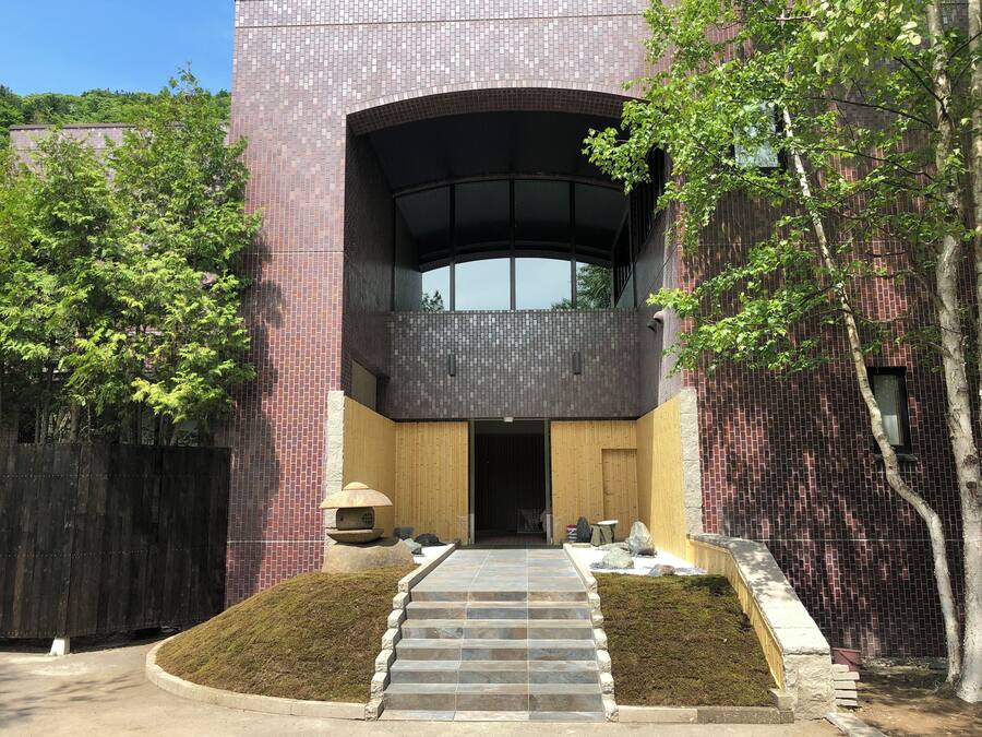 A modern building with a brick facade, a wooden entrance, and a curved balcony.